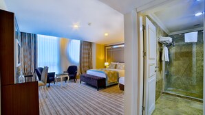 Habitación de hotel con cama, mesita de noche, silla y zona de ducha.