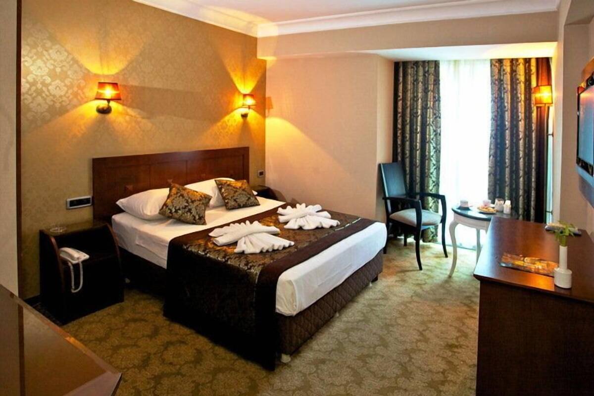 A hotel room with a large bed, two wall-mounted lamps, a desk with a chair, and a TV on the wall.