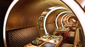 A luxurious dining car with a curved wooden interior, patterned seating, and a long table set for a meal. - The Deltin Hotel (Daman)