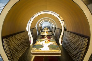 Un comedor con una mesa larga, varios asientos y un diseño de pared con motivos.