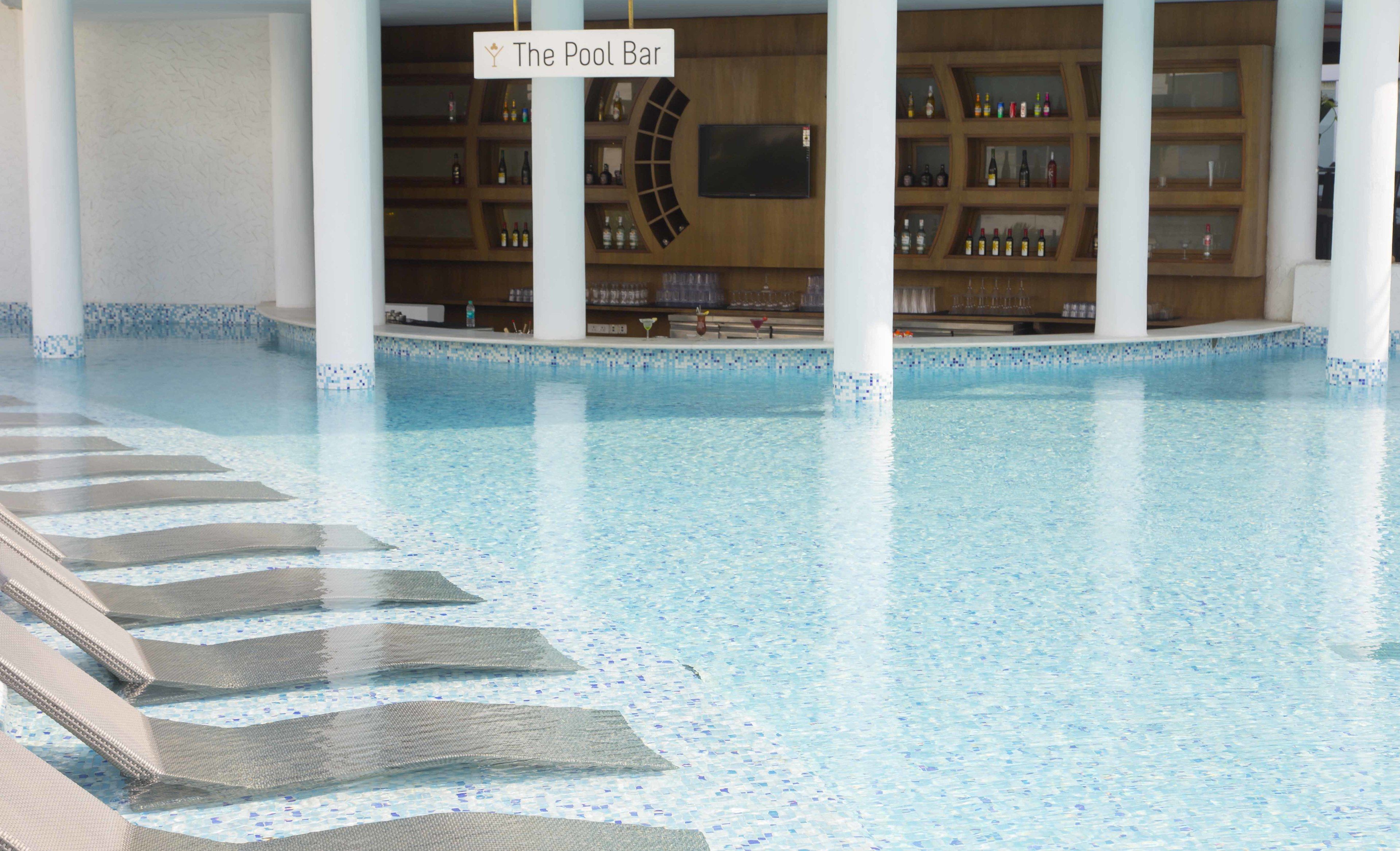 A pool area with a bar labeled "The Pool Bar" and a tiled pool with lounge chairs.