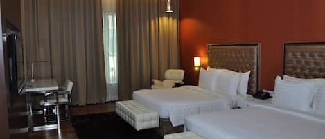 A hotel room with two beds, a desk, a chair, and a large window with curtains.