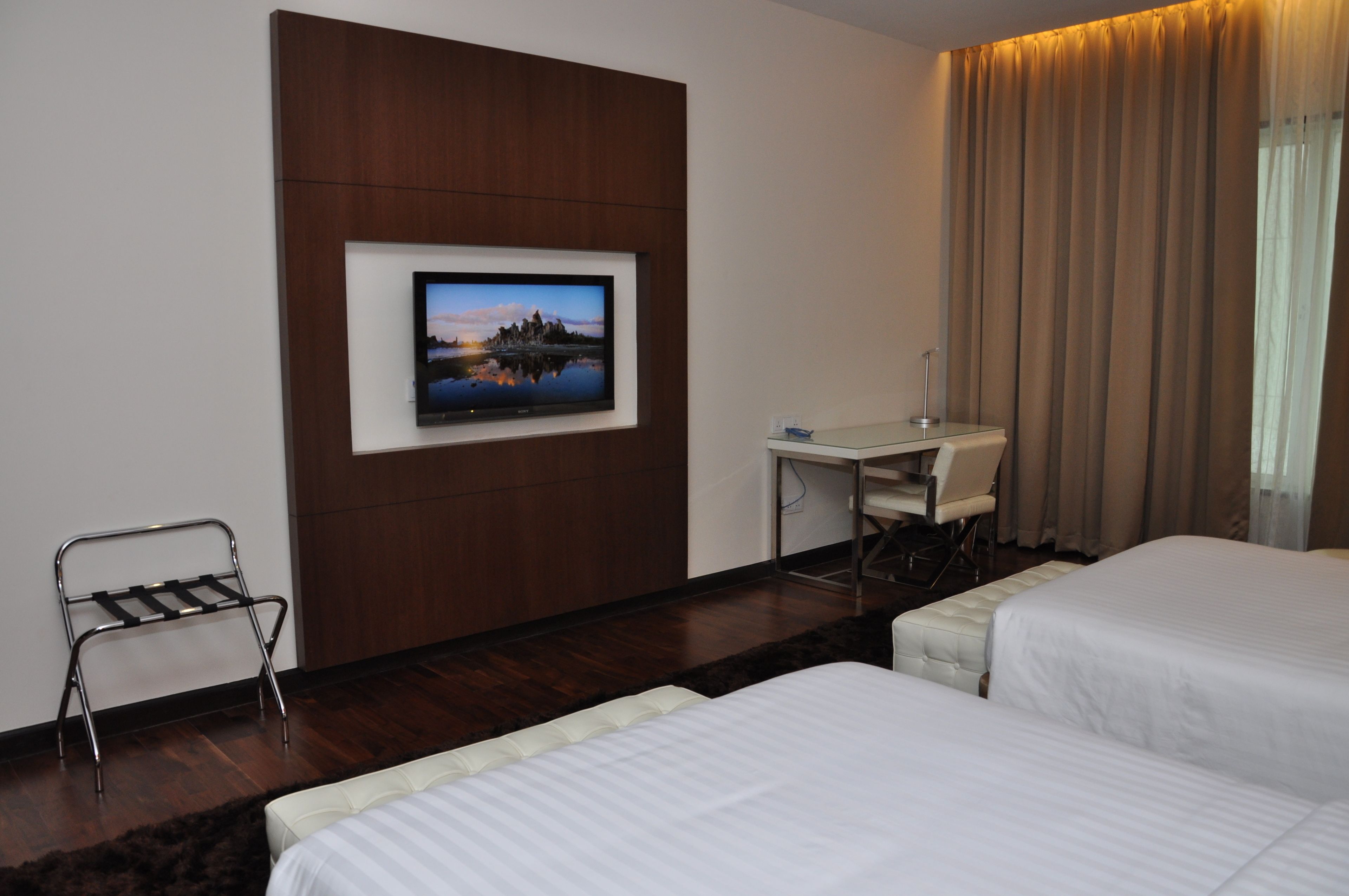 A hotel room with two beds, a desk, a TV mounted on the wall, and a chair.