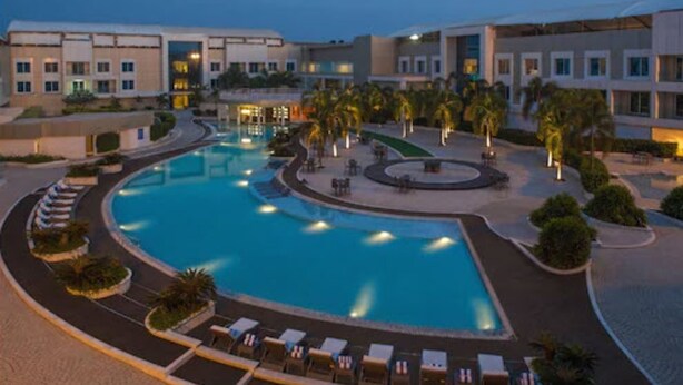 A resort pool area with a circular pool, lounge chairs, and palm trees. - The Deltin Hotel (Daman)
