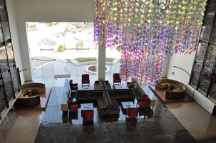 Um lobby moderno com piso de mármore refletivo, área de estar central com sofás e mesas, e uma grande janela com vista para a área externa.