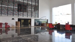 A spacious lobby with a polished marble floor, red and brown seating, and a large window providing natural light. - The Deltin Hotel (Daman)
