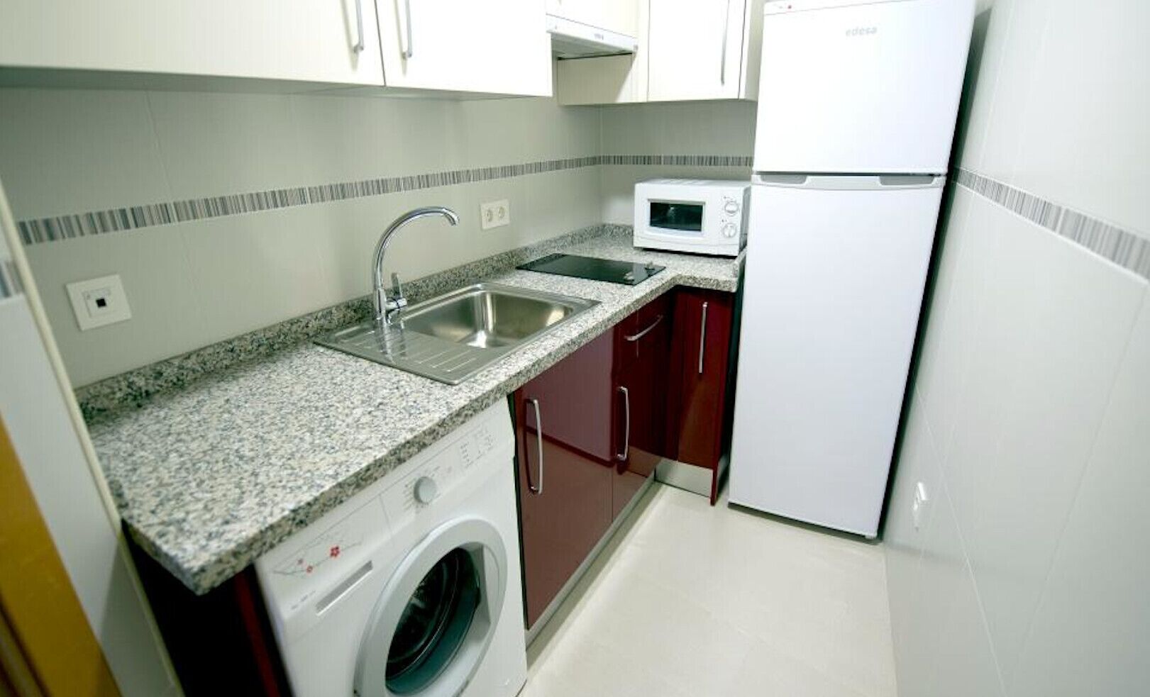 Una cocina compacta con lavadora, microondas, refrigerador y pileta.