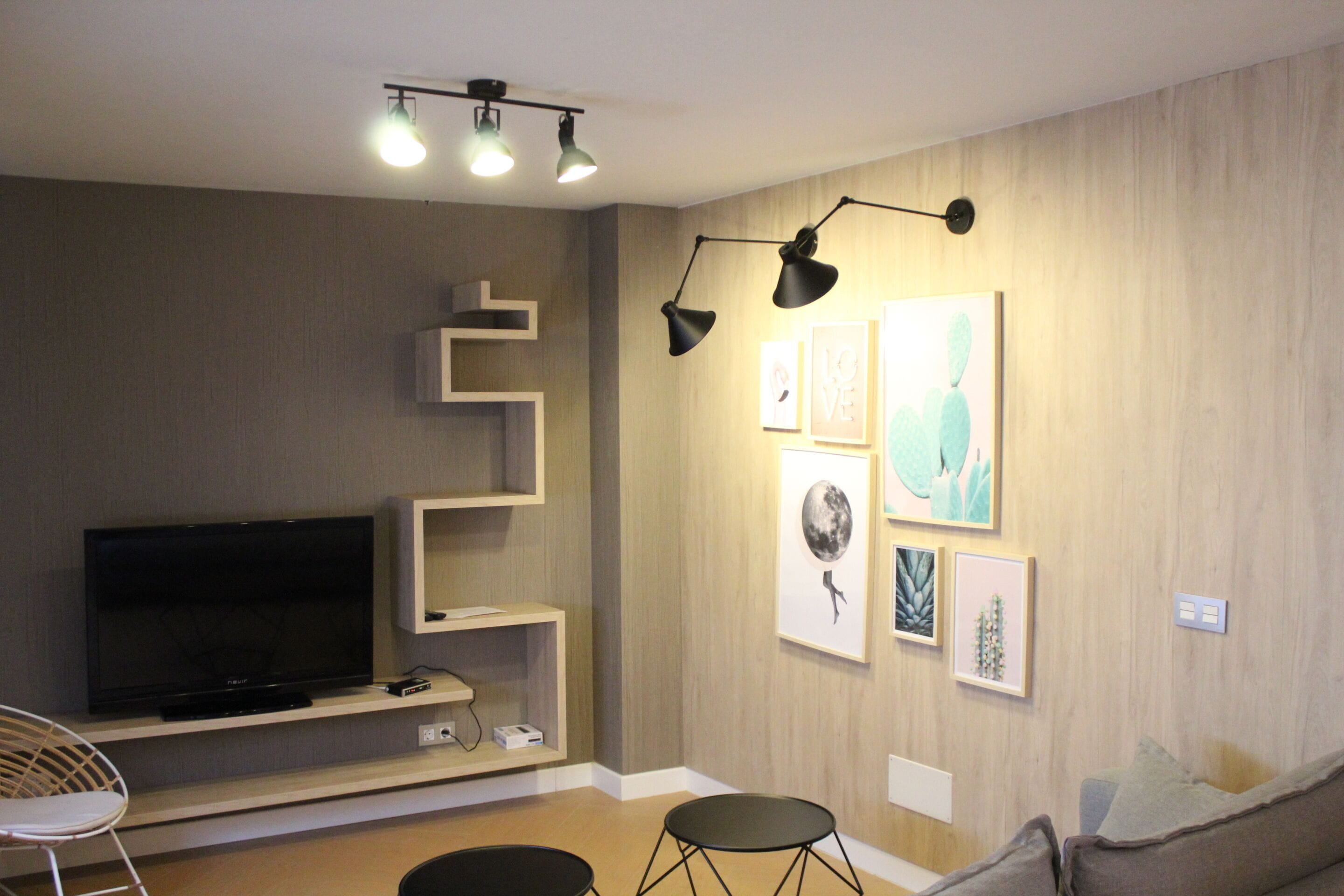 A modern living room with a flat-screen TV, a sofa, a chair, and artwork on the walls.