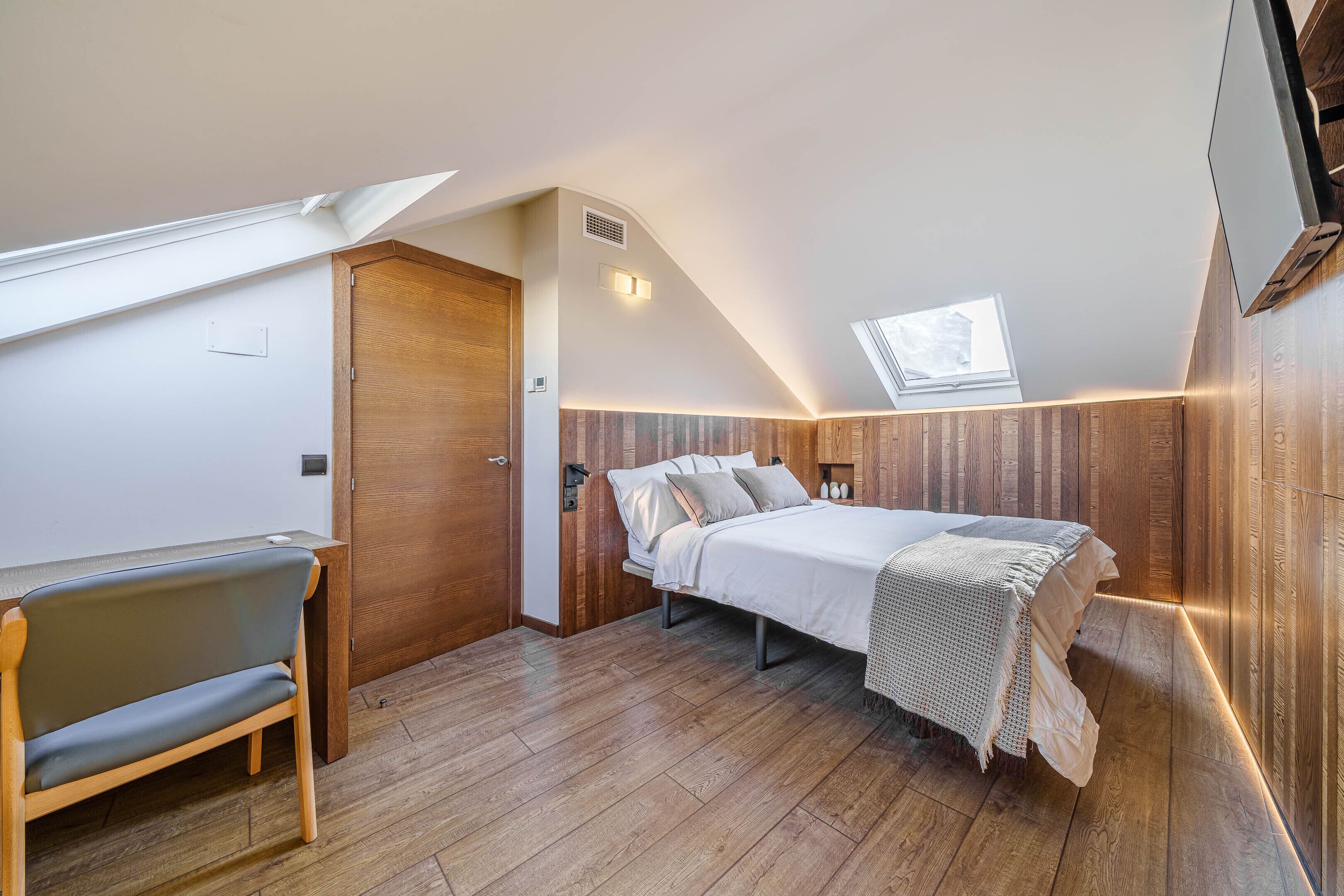 Un dormitorio con techo inclinado, una cama, un banco y un tragaluz.