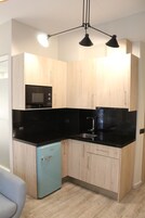 A compact kitchen with wooden cabinets, a black countertop, a blue refrigerator, and a modern pendant light fixture.
