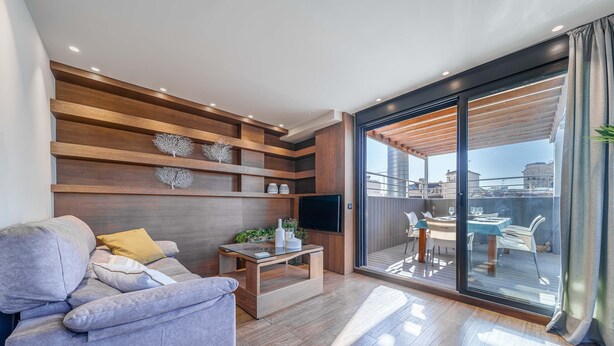 Una sala de estar moderna con sofá, mesa de centro y televisor, una pared de madera con estanterías y un ventanal corredero que da a un espacio exterior.