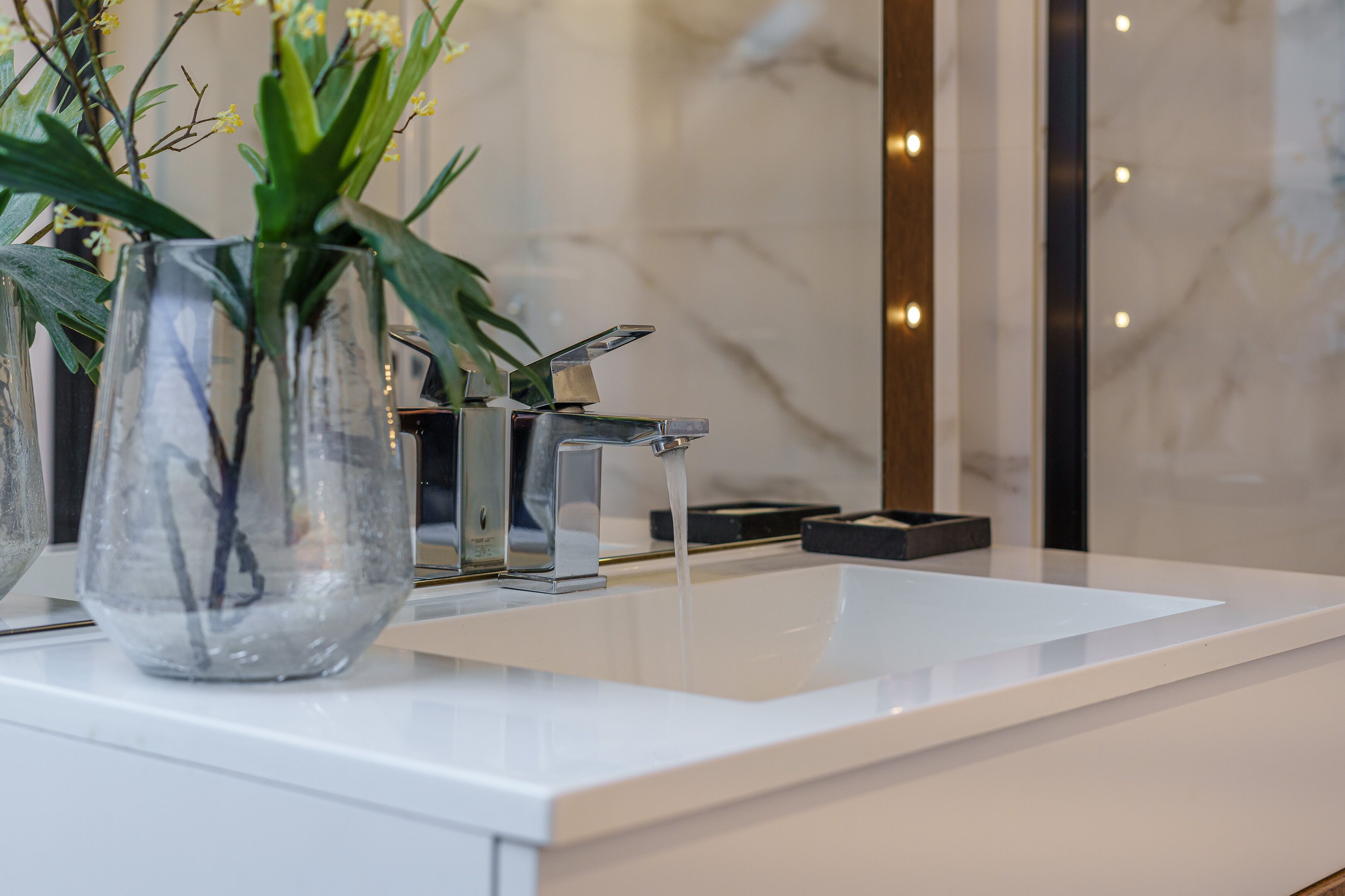 Un baño moderno con un lavamanos blanco, un grifo cromado y un florero con plantas verdes.