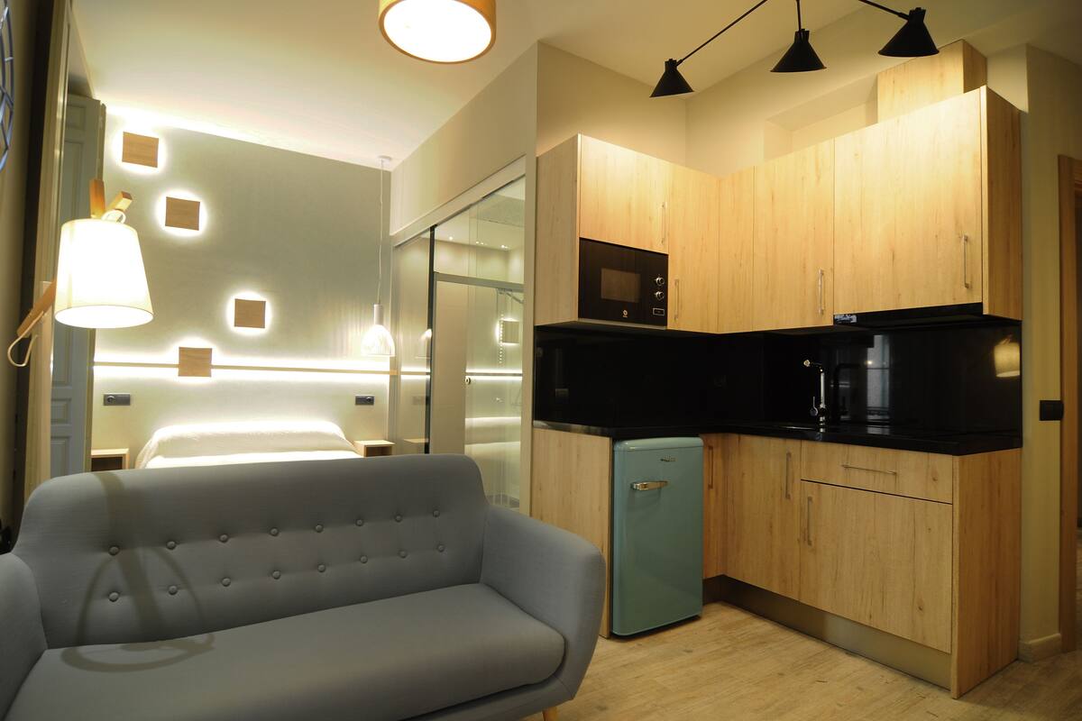 Un espacio habitable compacto con sofá, kitchenette y una puerta de vidrio que da al baño.