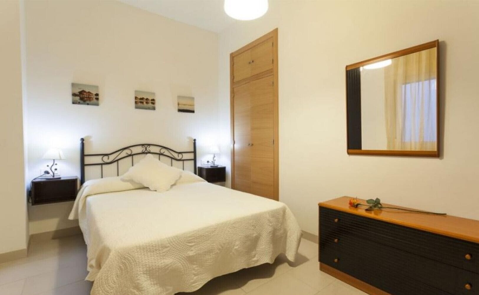 A bedroom with a bed, bedside tables, a dresser, a mirror, and a wardrobe.