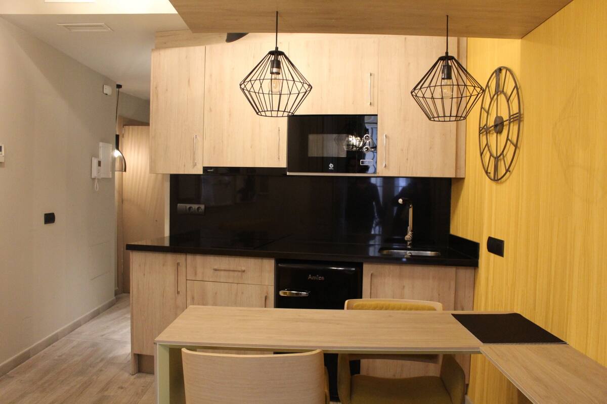 Una cocina moderna con armarios de madera, encimera negra y dos lámparas colgantes.