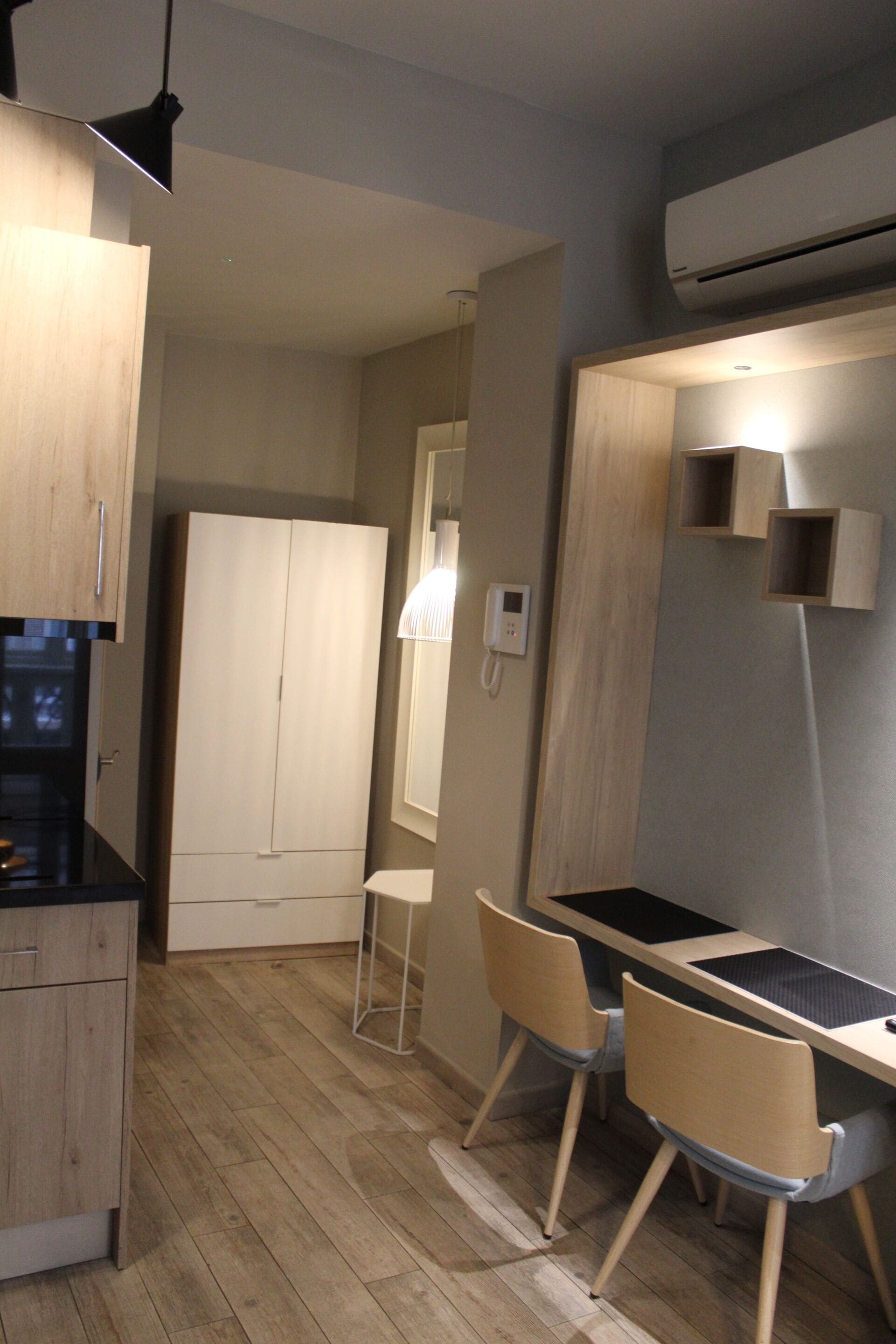 A compact kitchen with wooden cabinets, a black countertop, and a built-in stove. There is a small dining area with a table and two chairs.