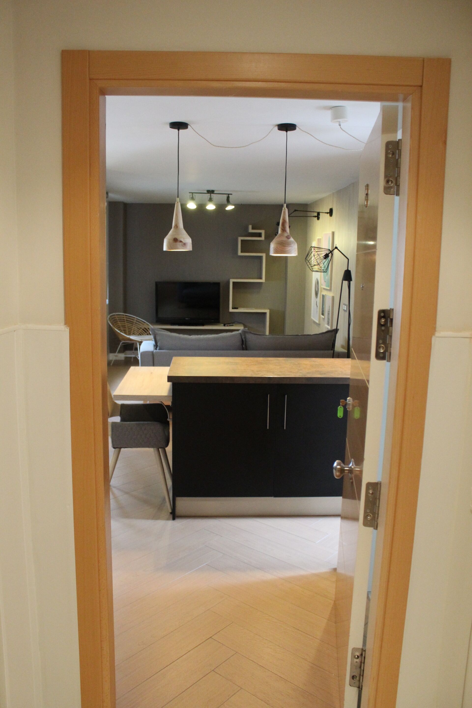 A modern kitchen with a dining area, featuring a wooden table, black cabinets, and pendant lighting.