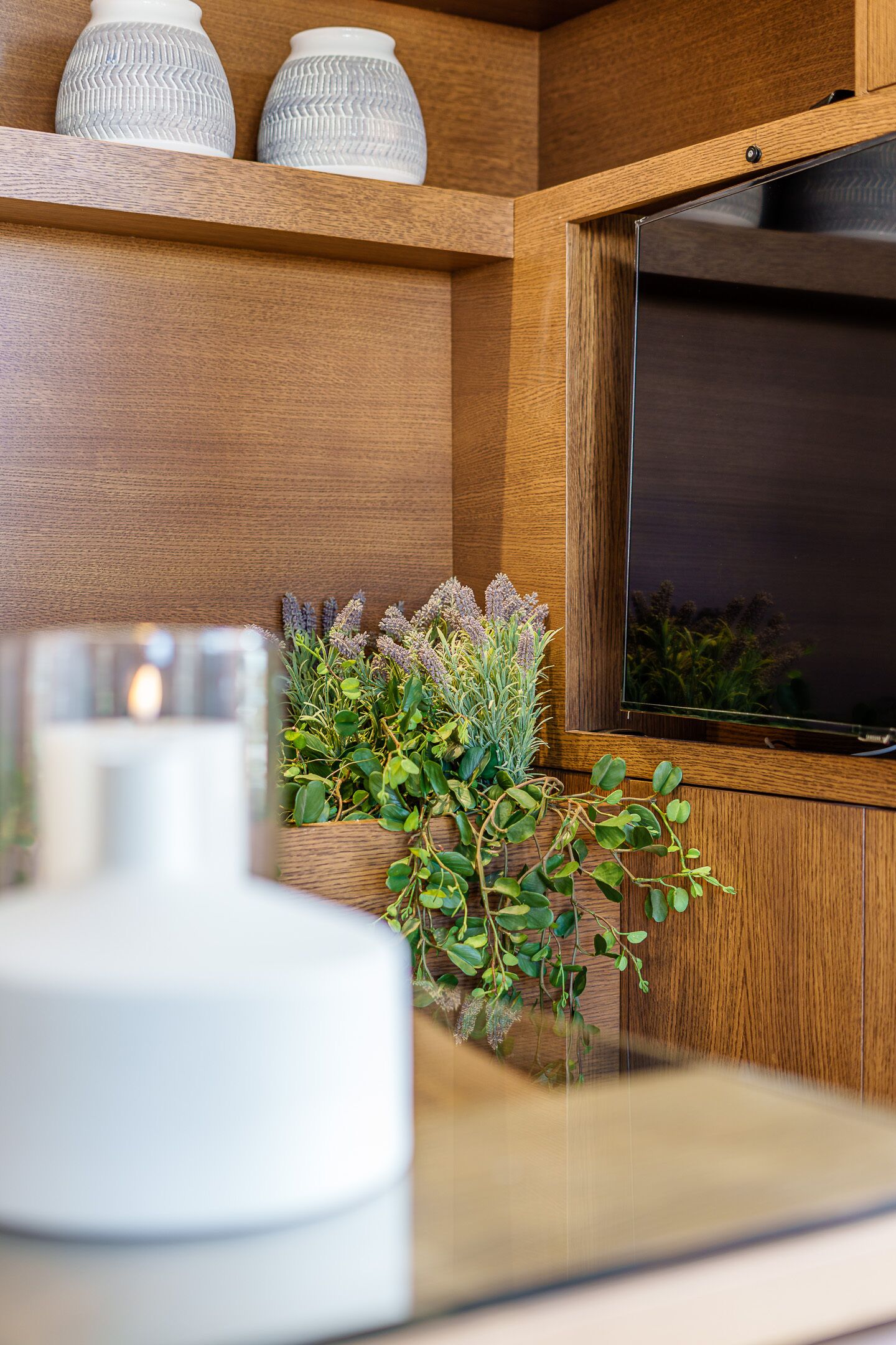Un interior de madera con una televisión montada en la pared, una vela blanca y plantas decorativas.