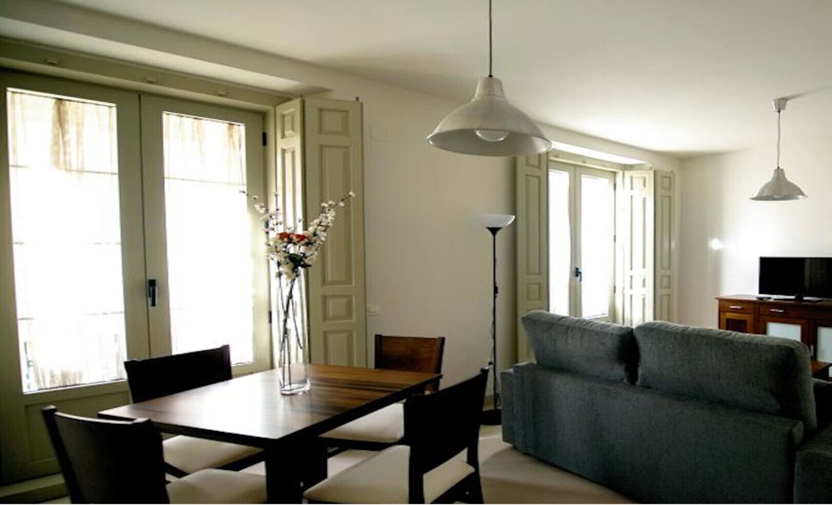 Un comedor con una mesa y sillas de madera, un florero con flores y un sofá gris.