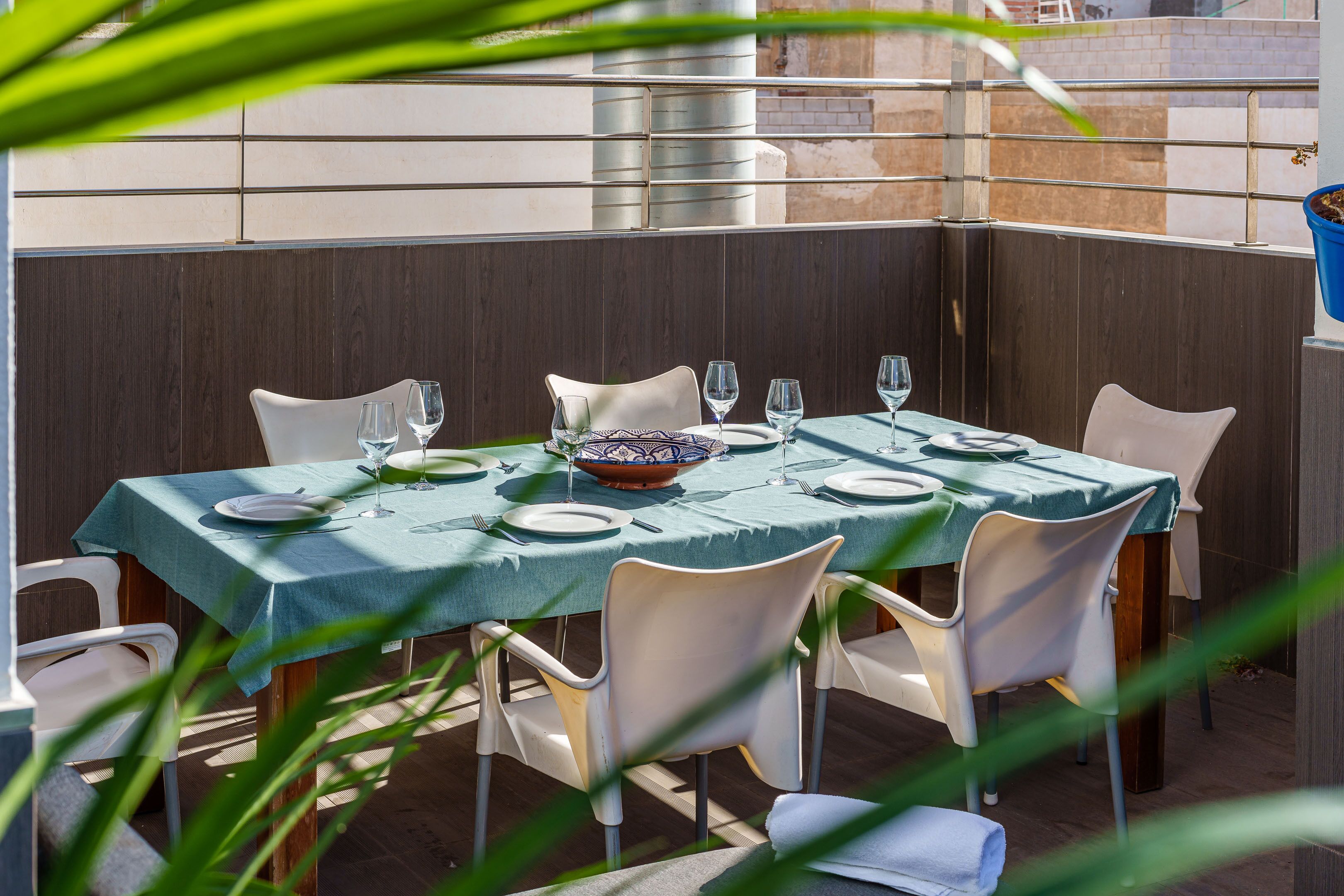 An outdoor dining area with a table set for four, surrounded by white chairs, and a blue tablecloth.