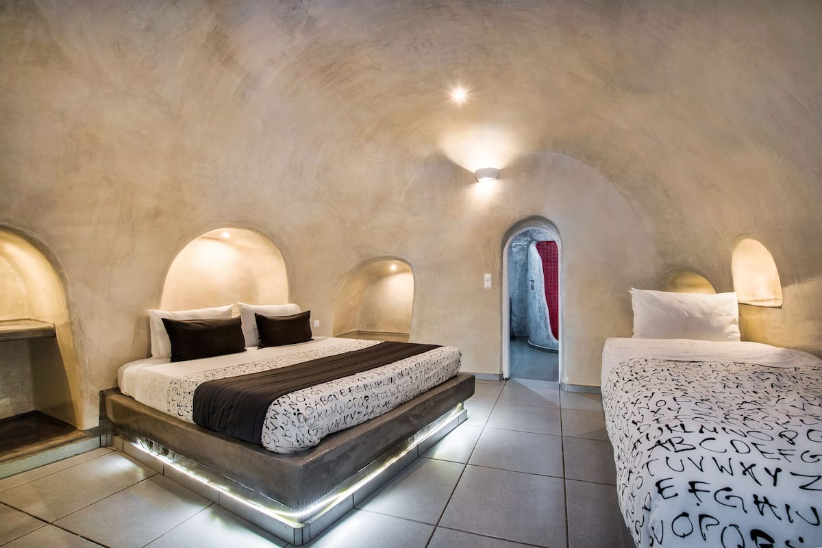 A bedroom with a unique arched ceiling, a bed with patterned bedding, and a bedside table.
