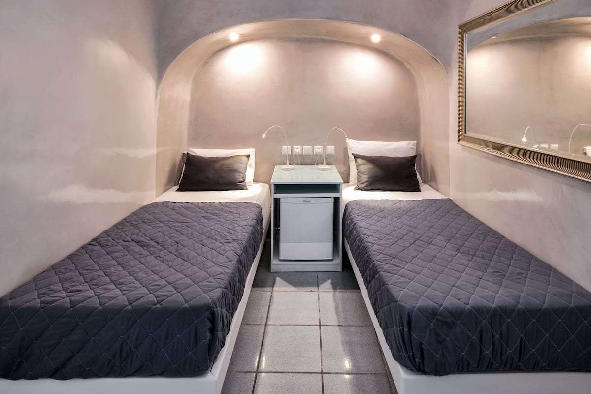 A compact room with two single beds, a small bedside table with a lamp, and a mirror on the wall.
