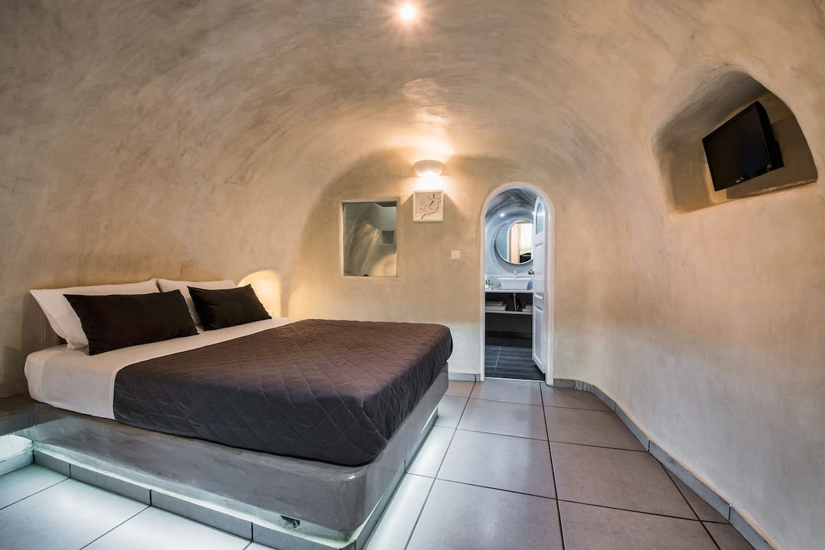 A bedroom with a bed, a TV, and a bathroom visible through an archway.