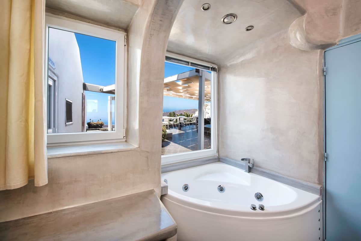 A modern bathroom with a large bathtub, a window with a view of the outdoors, and a shower area.