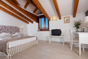 Quarto com uma cama, uma escrivaninha e uma cadeira. Há uma janela com vista para as montanhas.