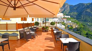 Une terrasse avec des sièges extérieurs, un grand parasol et une vue sur un paysage montagneux.