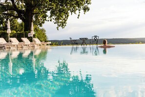 A pool with lounge chairs and a table, surrounded by trees and a view of the landscape. - Hotel & Spa Der Steirerhof Bad Waltersdorf (Bad Waltersdorf)