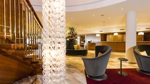 A hotel lobby with a staircase, a decorative column, seating area, and a reception desk. - Hotel & Spa Der Steirerhof Bad Waltersdorf (Bad Waltersdorf)