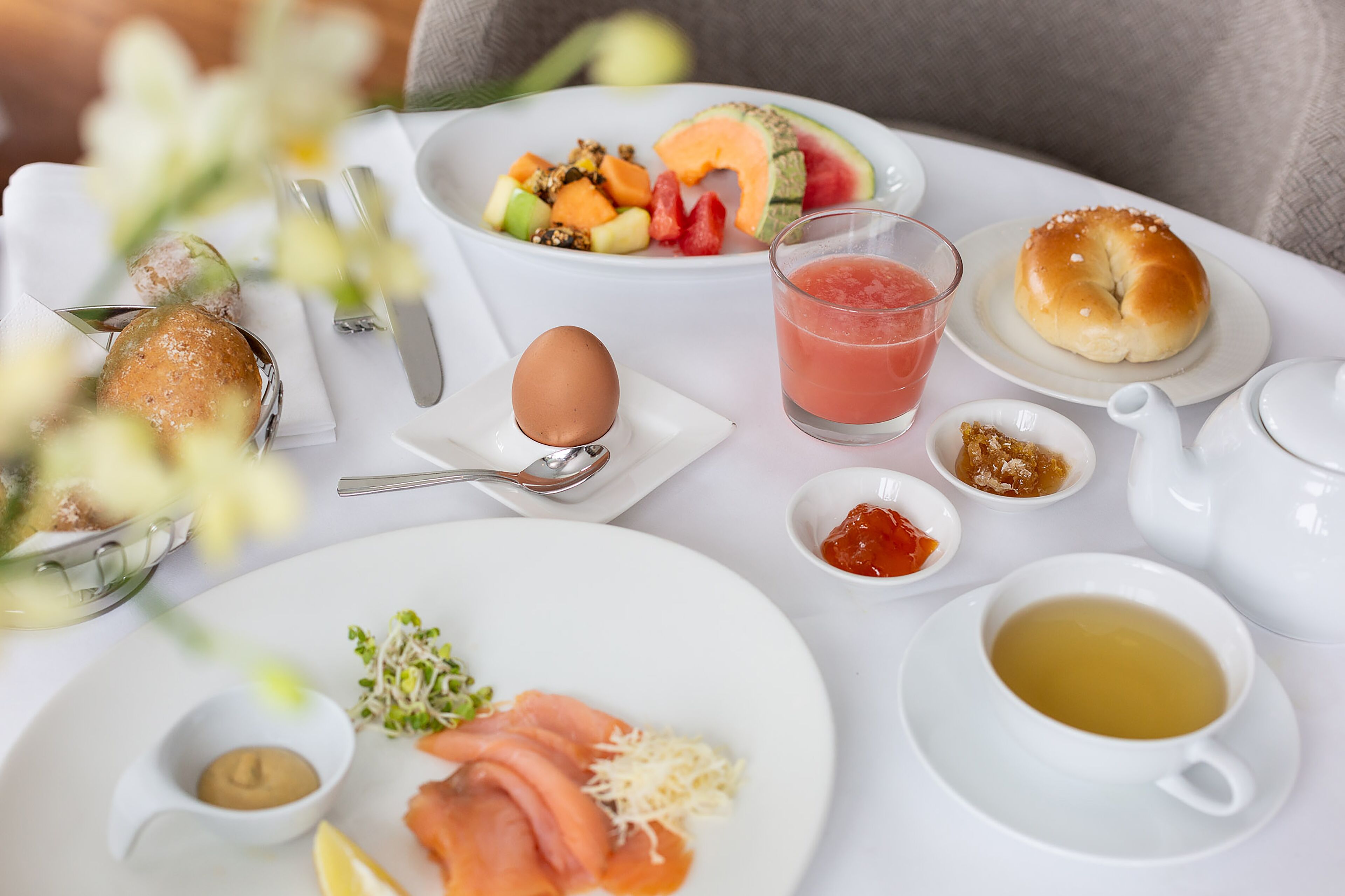 A breakfast setting with a variety of food items including fruits, a bagel, eggs, and beverages.