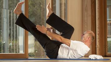 A person performing a yoga pose on a mat in a room with large windows and wooden doors.