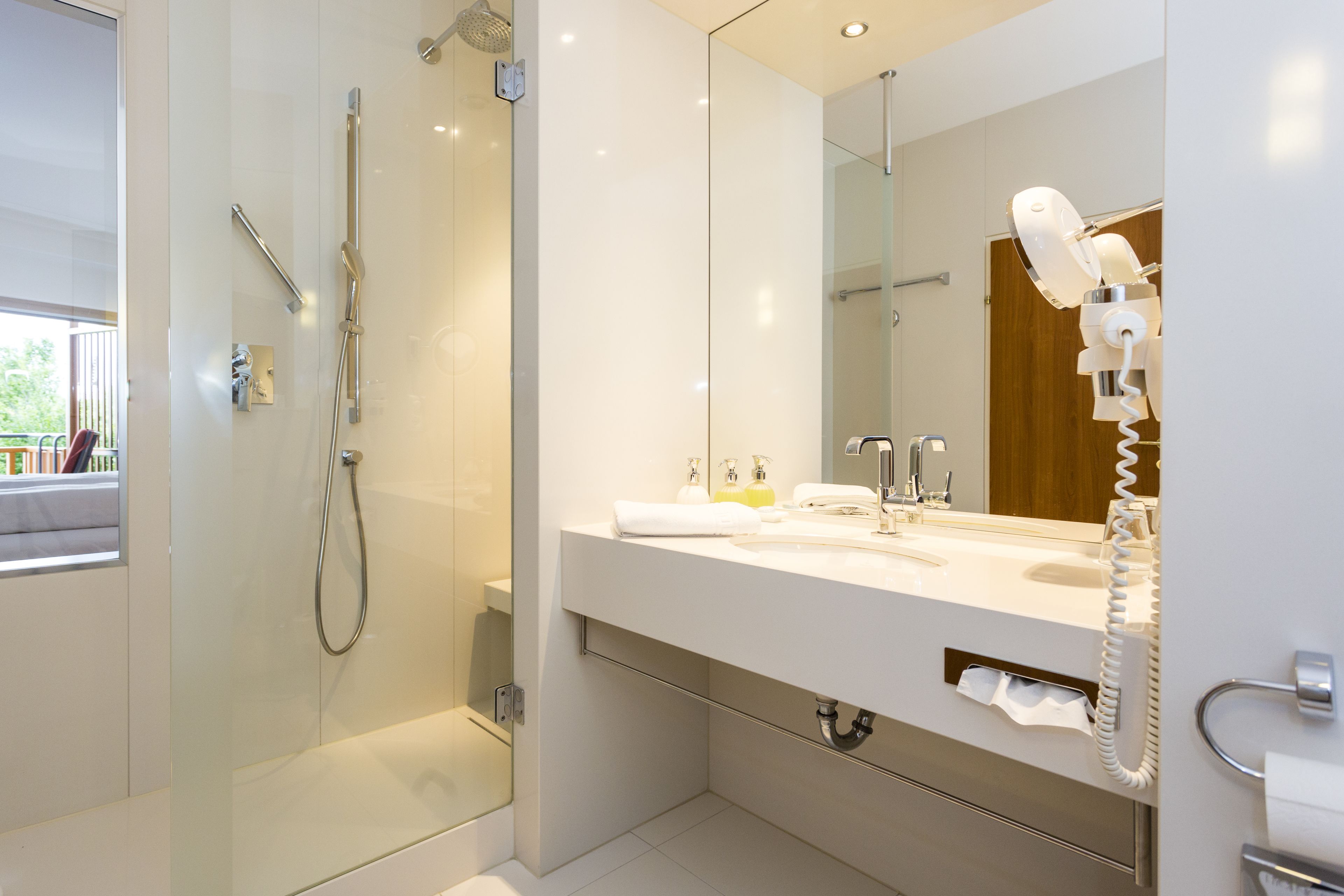 A modern bathroom with a glass-enclosed shower, a large mirror, a white sink, and a hairdryer mounted on the wall.