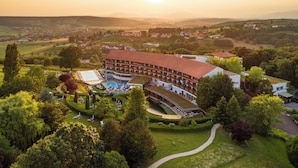 A large hotel with a swimming pool, surrounded by lush greenery and a scenic view of a town. - Hotel & Spa Der Steirerhof Bad Waltersdorf (Bad Waltersdorf)