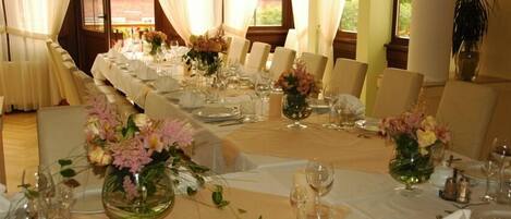 A formal dining room with long tables set for multiple guests, featuring white tablecloths, neatly arranged place settings, and floral centerpieces.