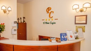 A reception desk with a wooden finish, a logo with 'PC' and 'V Para Cogito' on the wall, a framed certificate, and a bulletin board with informational cards. - U Pana Cogito (Kraków)