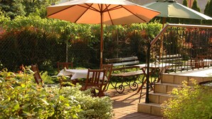 An outdoor patio area with a wooden bench, a table with a white tablecloth, and a large umbrella providing shade. - U Pana Cogito (Kraków)