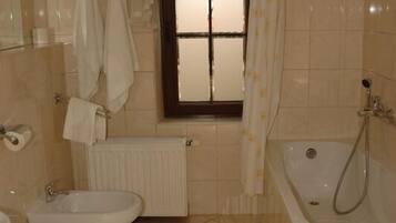A bathroom with two toilets, a sink, a bathtub, and a window with curtains.