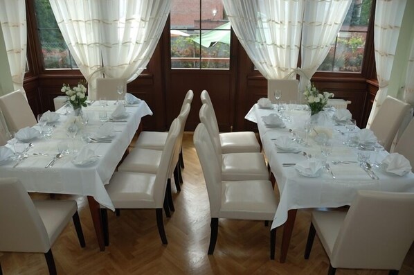 Un comedor con manteles y sillas blancas, y suelo de madera.