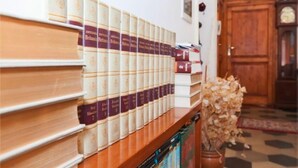 Una estantería con varias filas de libros, una puerta de madera y una planta en maceta al fondo.