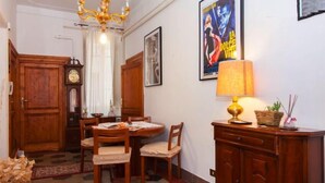 Un comedor con una mesa y sillas de madera, una araña, un reloj y un cartel en la pared.