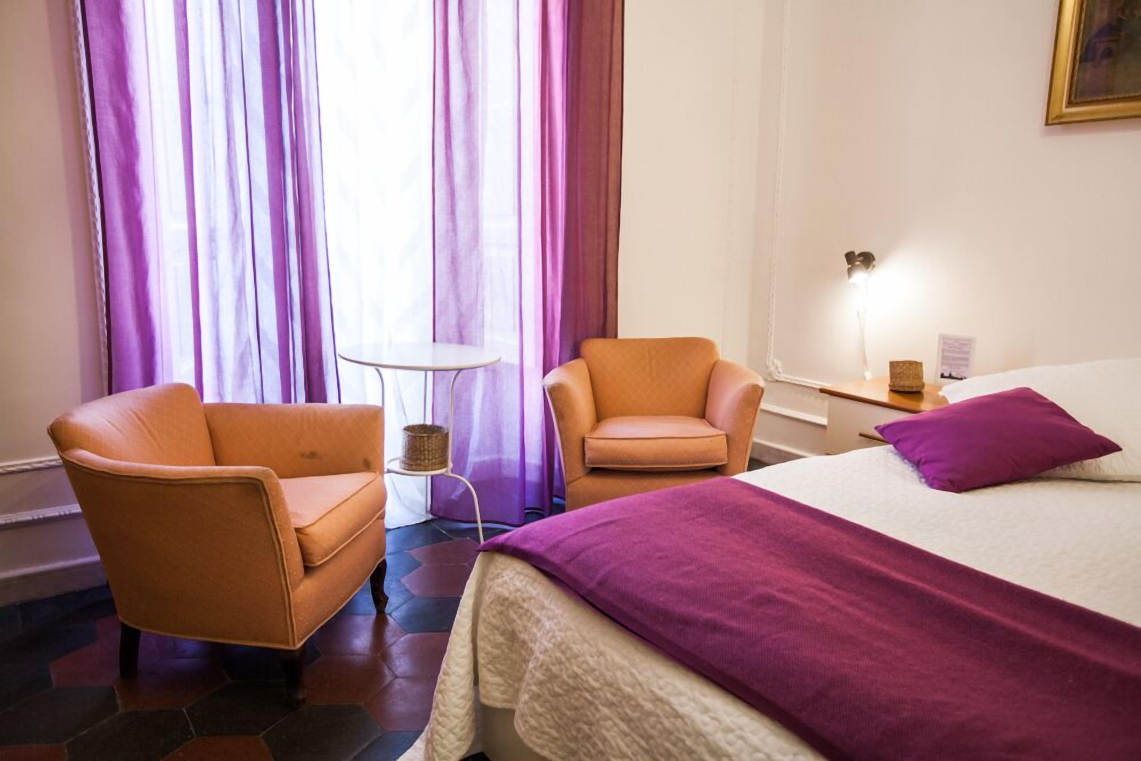 A hotel room with a bed, two armchairs, a small table, and a lamp.