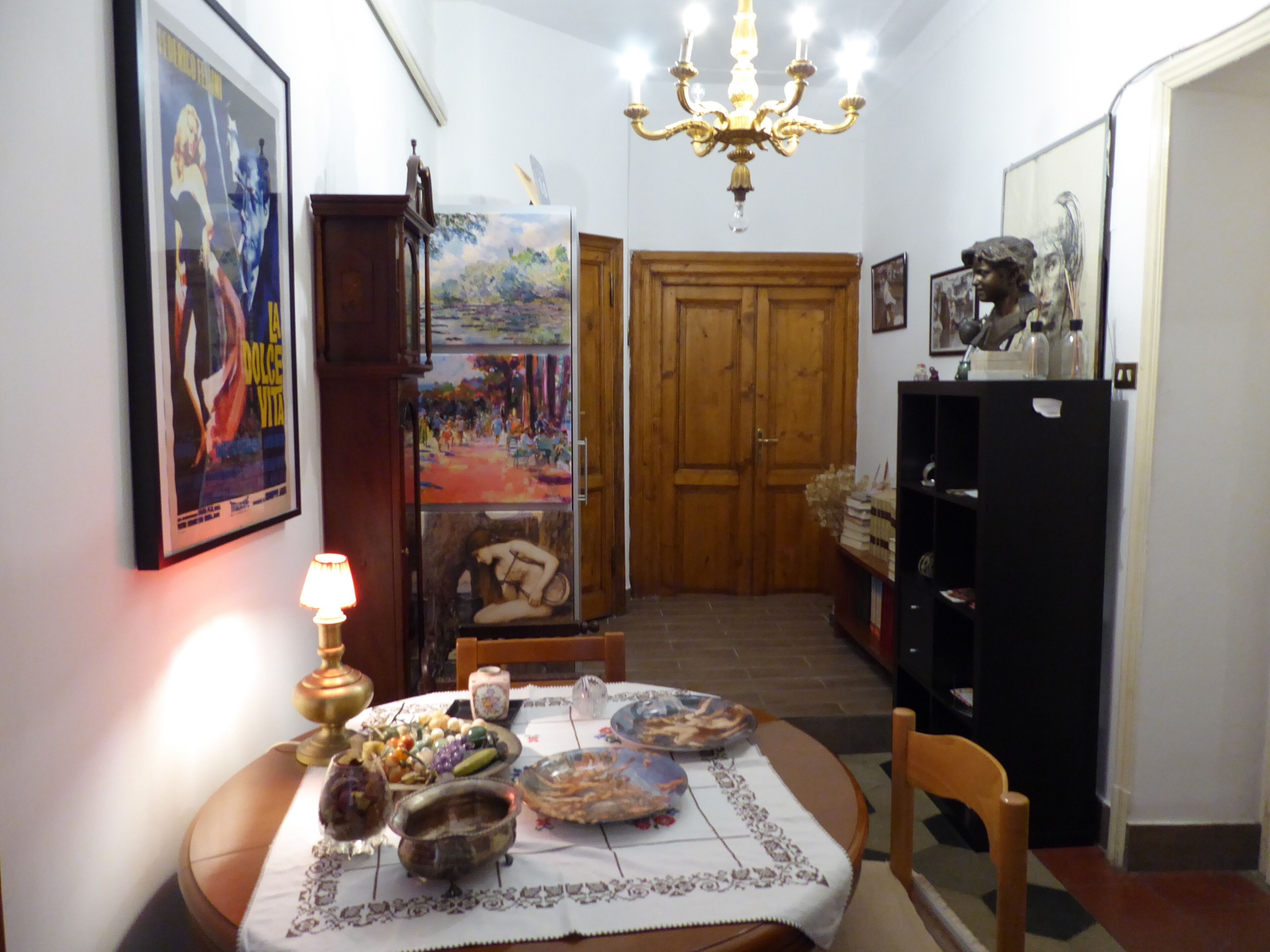 A dining area with a table set for two, a chandelier, a wooden door, and a bookshelf.