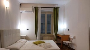 Una habitación de hotel con dos camas, un escritorio, una silla y un aire acondicionado.