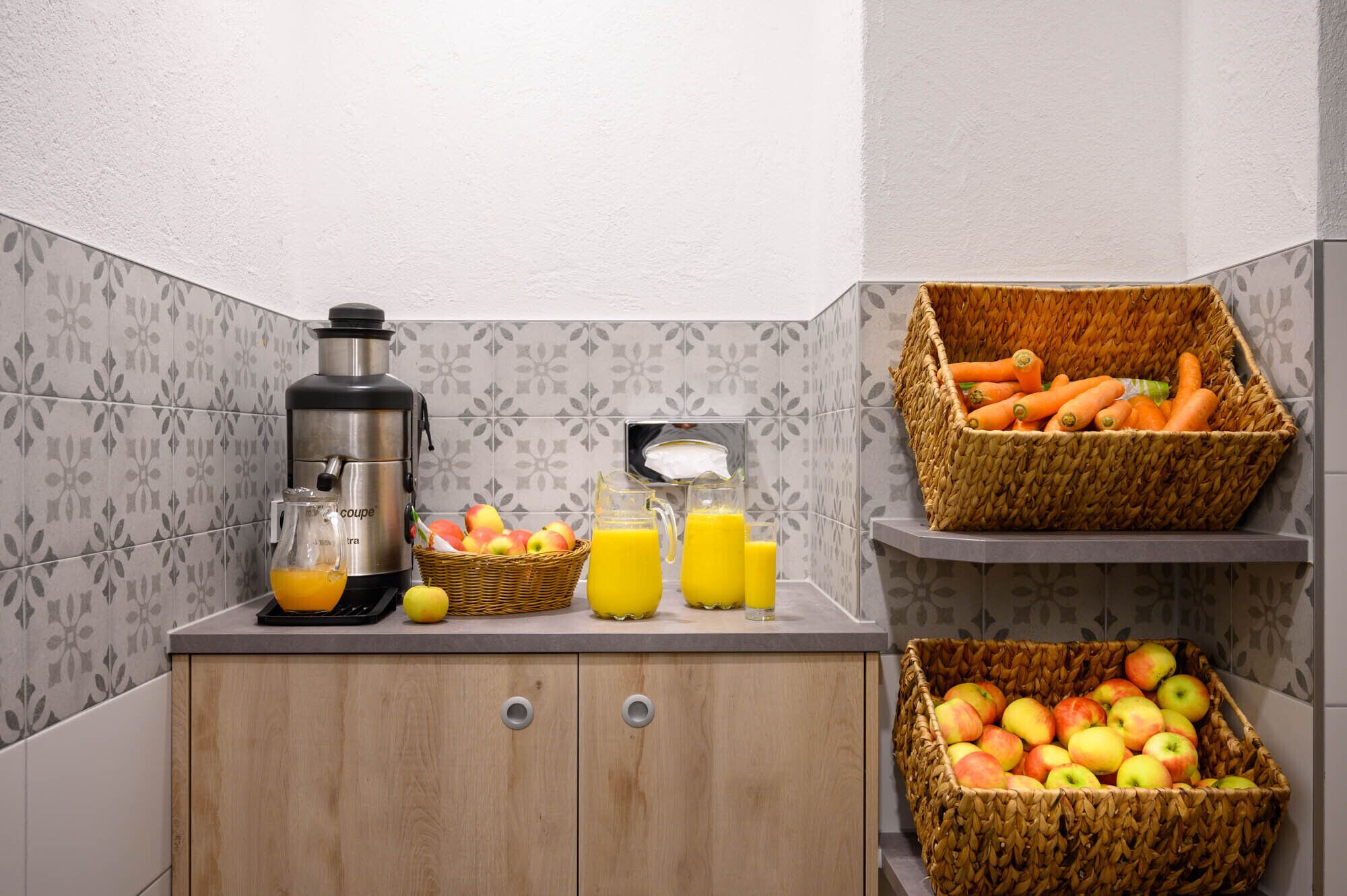 Une cuisine équipée d’une machine à café, d’un extracteur de jus et de paniers remplis de pommes et de carottes.