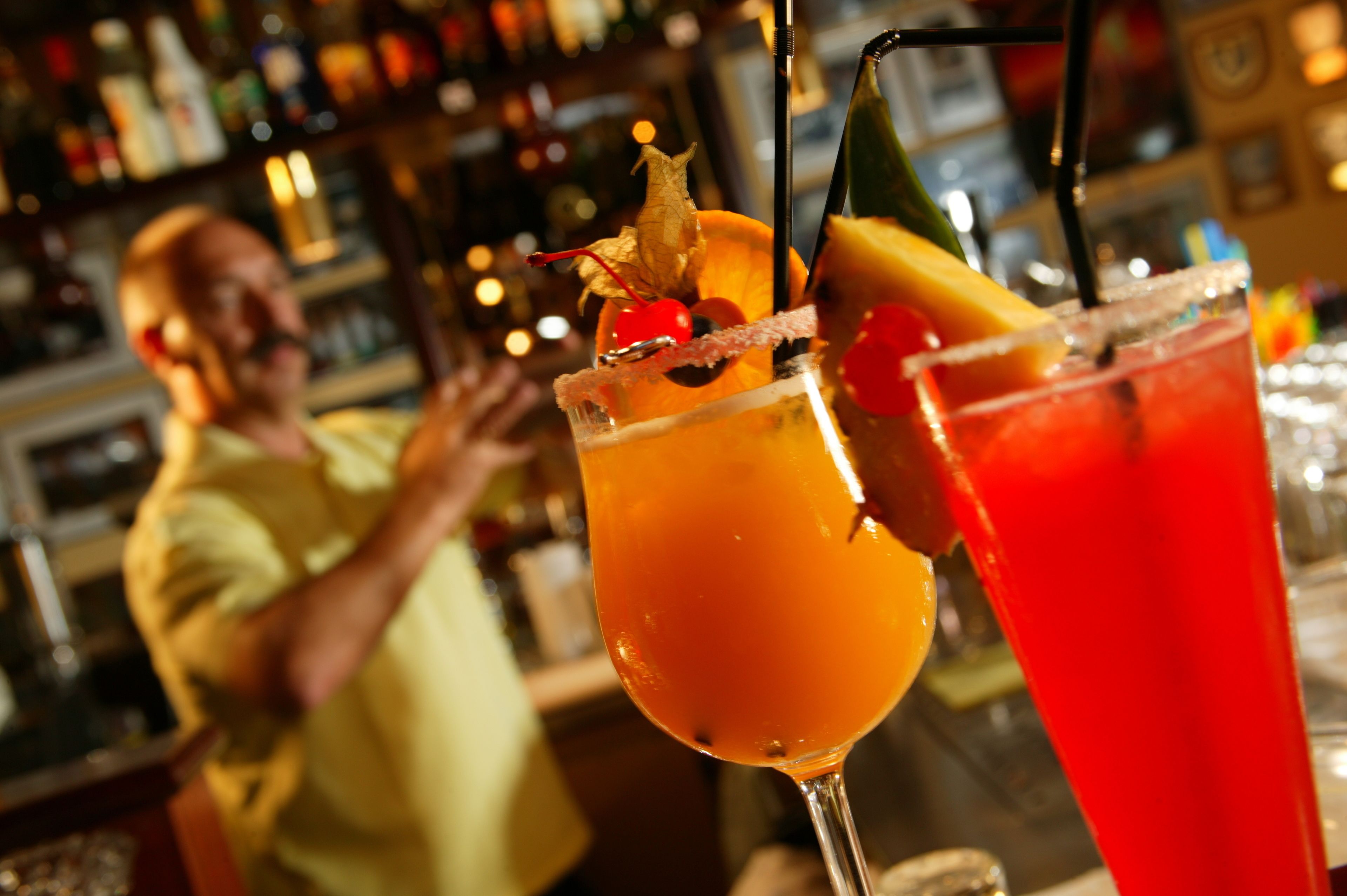 Un bar con dos cócteles adornados con frutas y una persona al fondo.