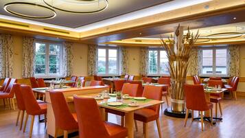 A dining area with multiple tables and chairs, large windows, and a decorative plant centerpiece.