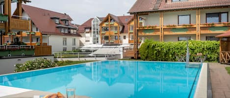 A swimming pool with a clear blue water surface, surrounded by wooden buildings with balconies and a small staircase leading to a second floor.